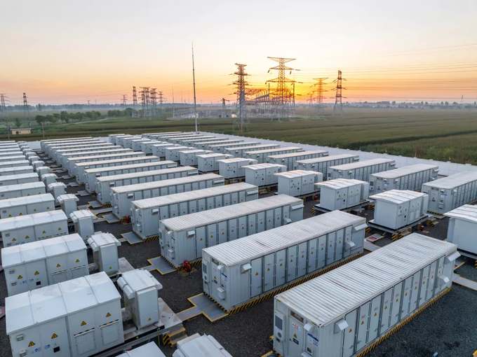Rows of grid-scale battery storage containers beside a substation — distributed assets aggregated into a virtual power plant